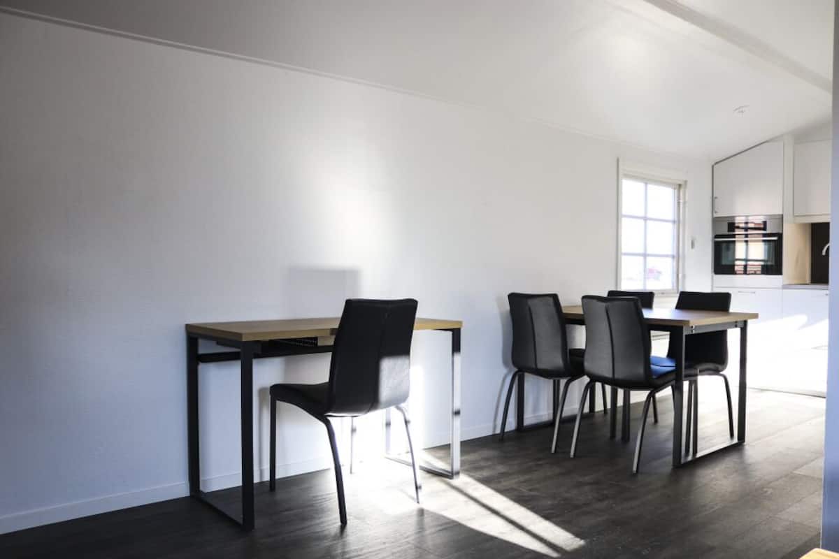 A modern kitchen with a dining area, featuring a wooden table and black chairs.