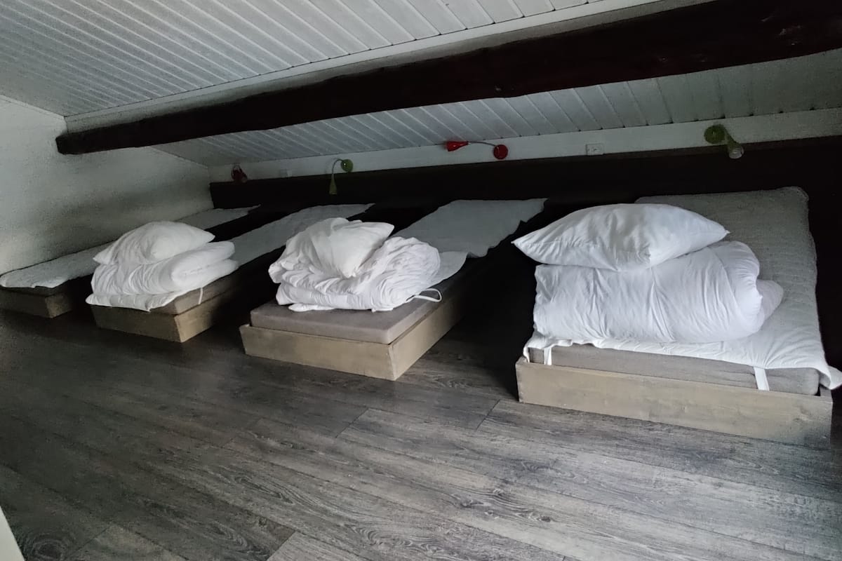 A dormitory room with three bunk beds, wooden flooring, and a sloped ceiling.