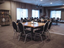 Un salón de conferencias con varias mesas y sillas, ventanas amplias y un sistema de sonido.