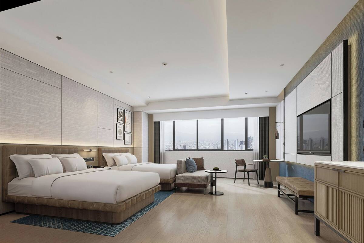 A modern hotel room with a large bed, a sofa, a small table, and a view of the city.