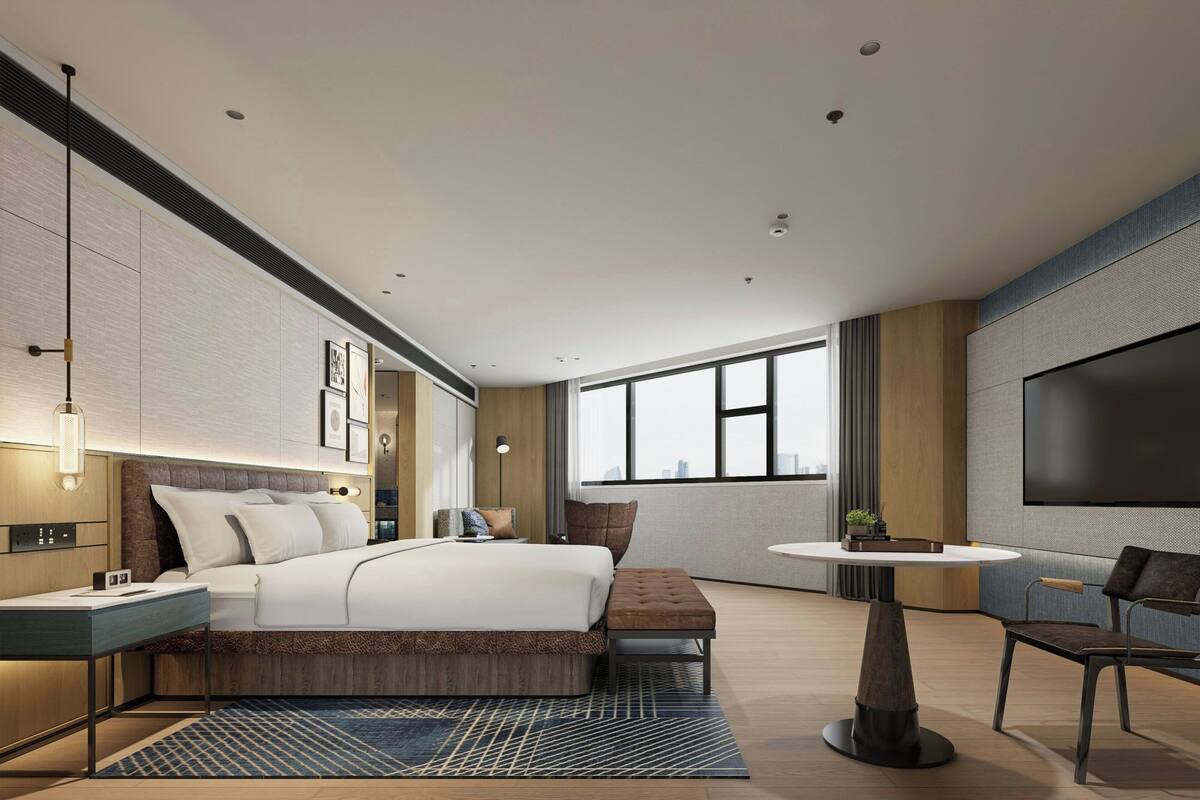 A modern hotel room with a large bed, a TV, a round table, and a view of the city.