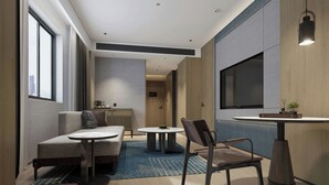 Une chambre d’hôtel moderne, équipée d’un canapé, d’une petite table ronde, d’une chaise, d’un grand téléviseur et offrant une vue sur la ville.