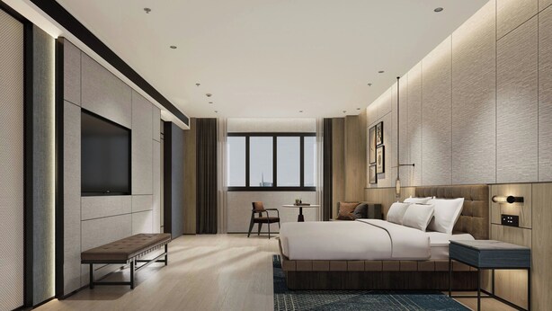 Une chambre d’hôtel moderne, dotée d’un grand lit, d’une banquette, d’une petite table et d’un téléviseur fixé au mur.