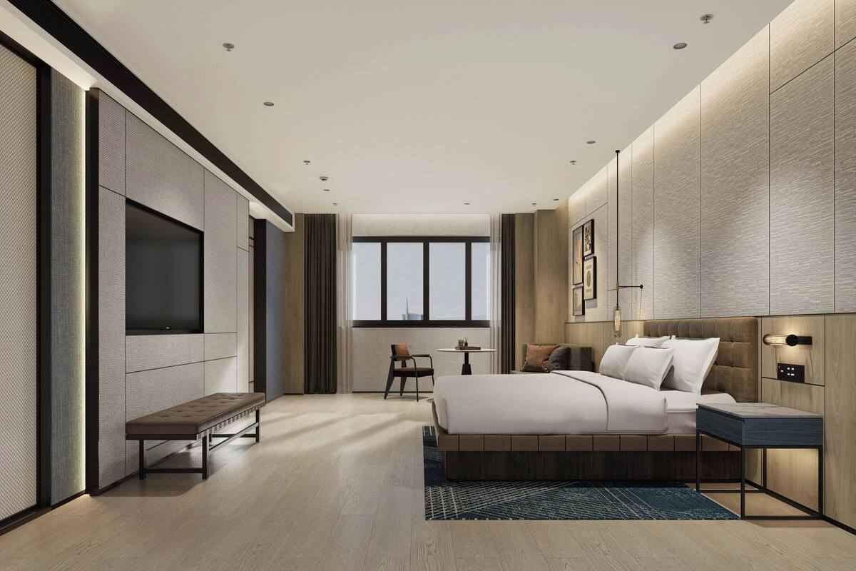 A modern hotel room with a large bed, a bench, a small table, and a TV mounted on the wall.