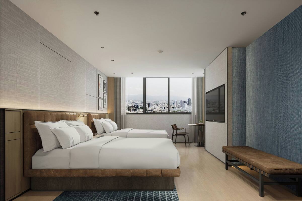 A modern hotel room with a large bed, a bench, a desk, and a city view.