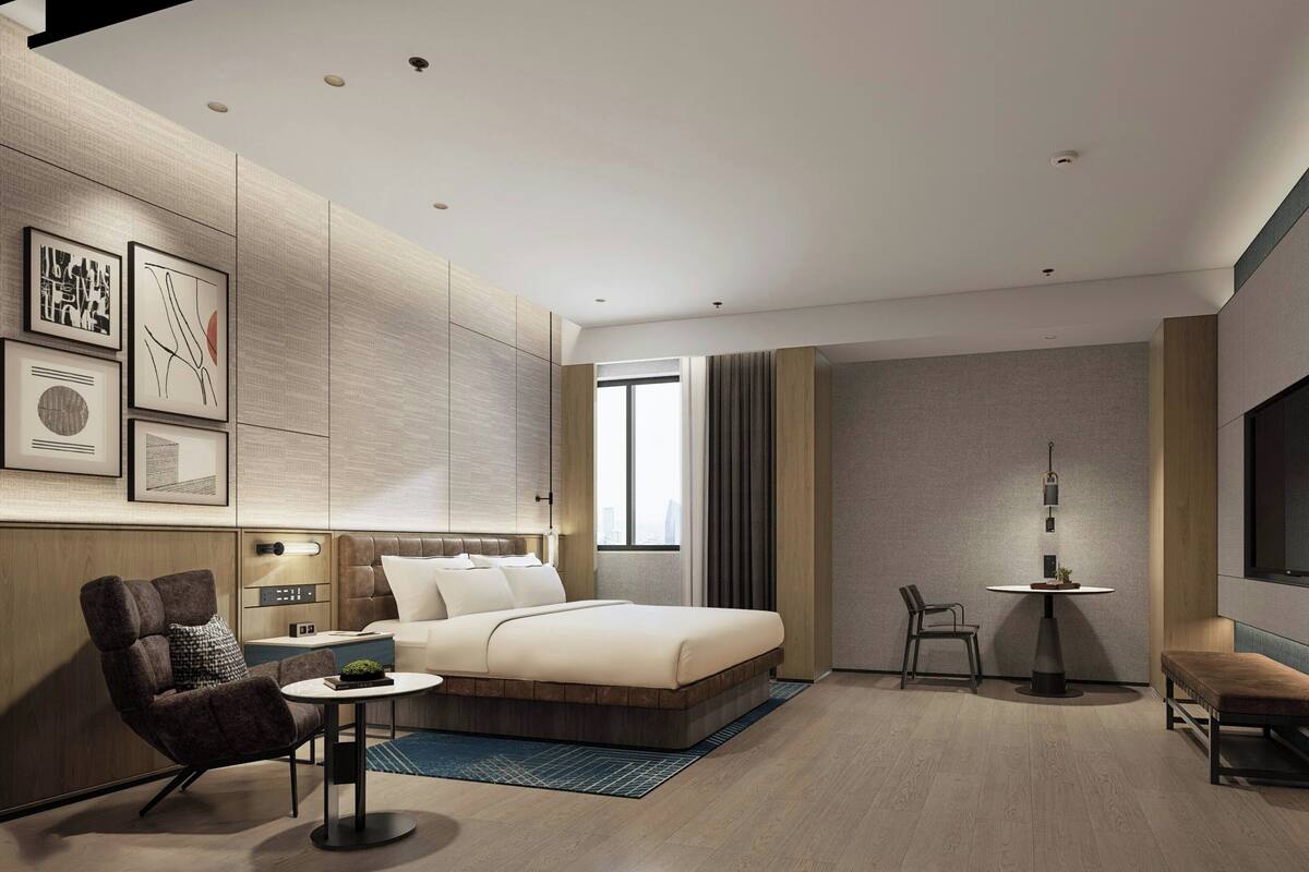 A modern hotel room with a bed, seating area, and a TV.