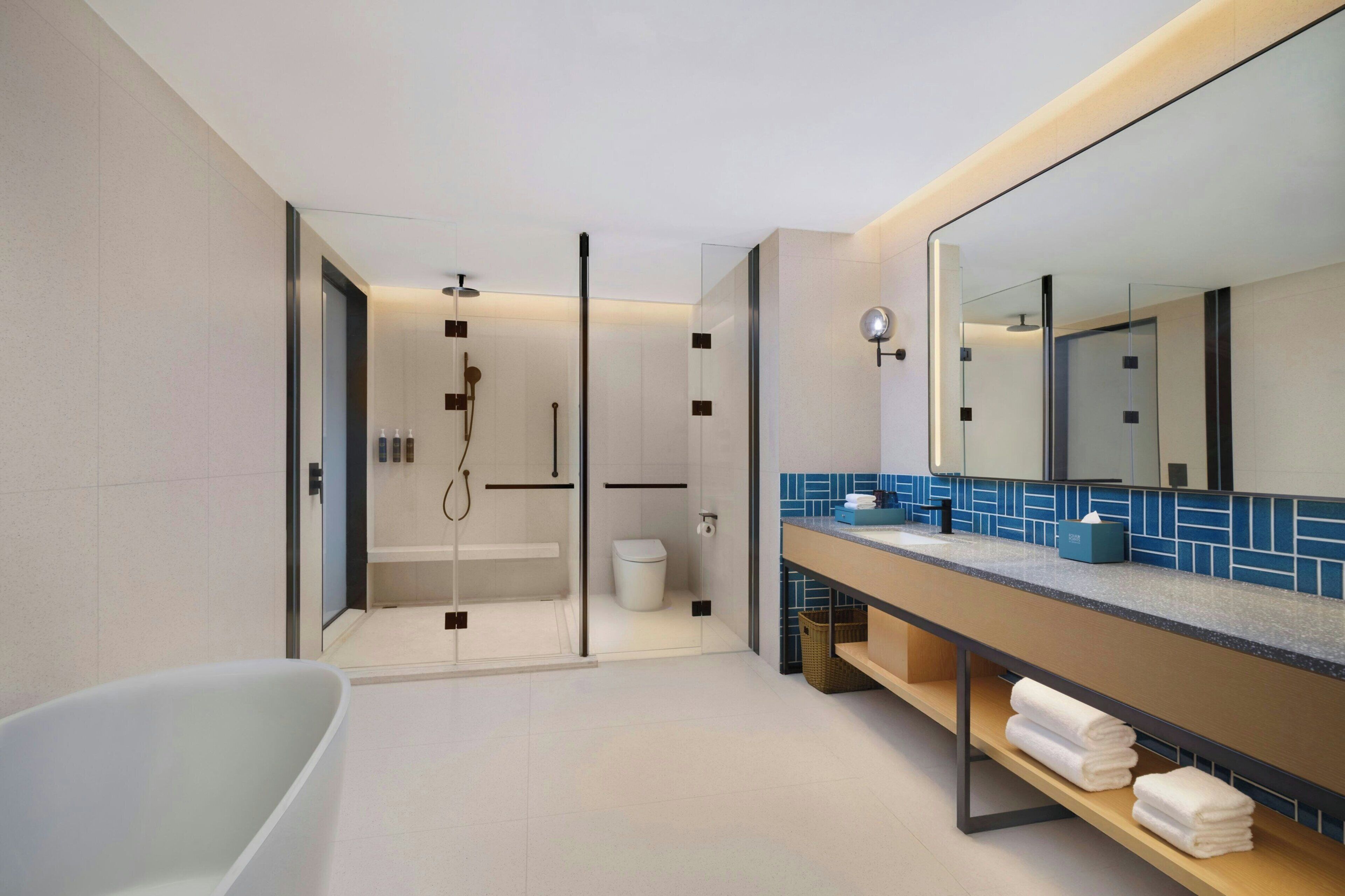 A modern bathroom with a glass-enclosed shower, a freestanding bathtub, and a vanity with a mirror and towel rack.