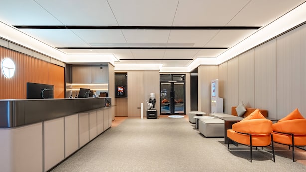 Een moderne hotellobby met een receptiebalie, een zithoek en uitzicht op de eetruimte.