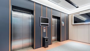Een lift met een digitaal scherm, noodknoppen en een afvalbak.