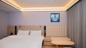 Een hotelkamer met een bed, nachtkastje, zithoek en een poster aan de muur.