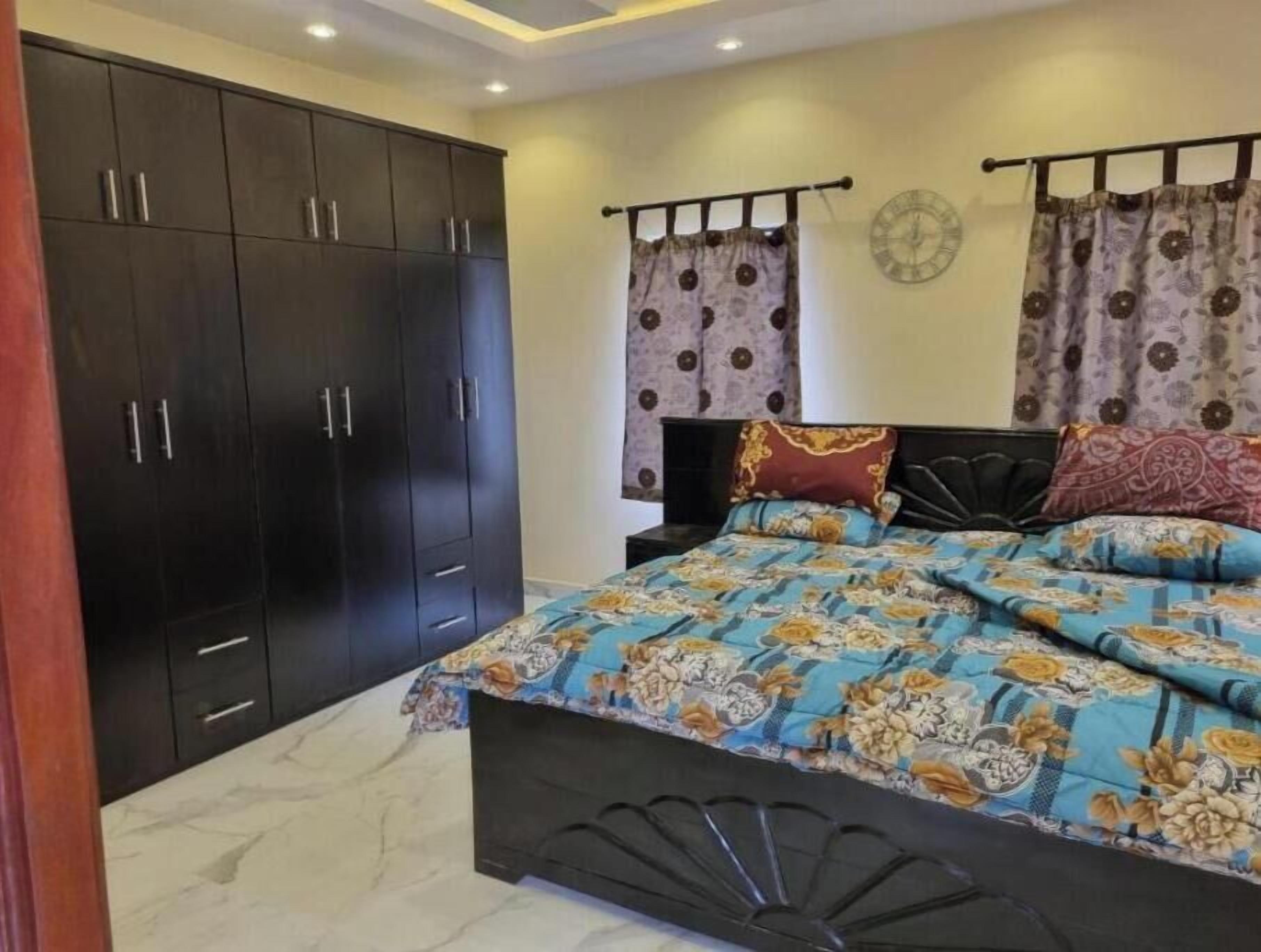 A bedroom with a bed, dark wooden wardrobe, and curtains.
