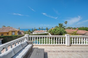 A balcony with a white balustrade, a wicker sofa, and a patterned floor.