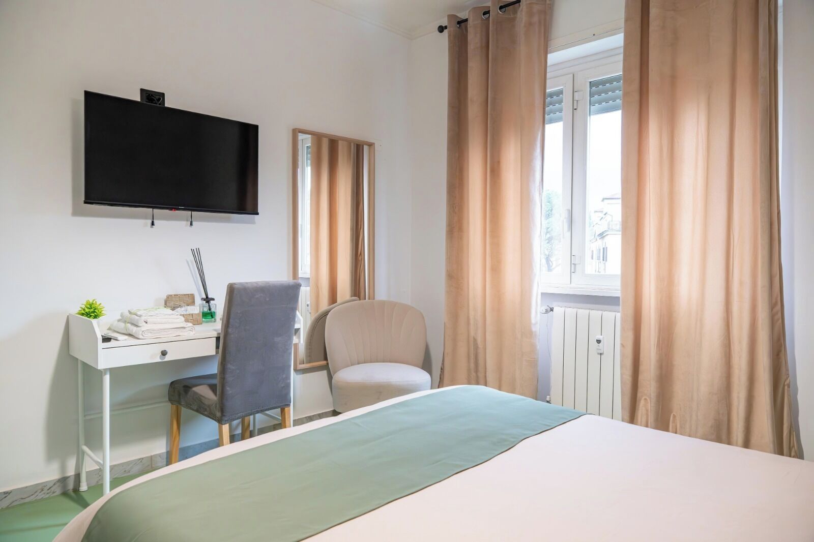 A hotel room with a bed, a desk with a chair, a television, and a window with curtains.