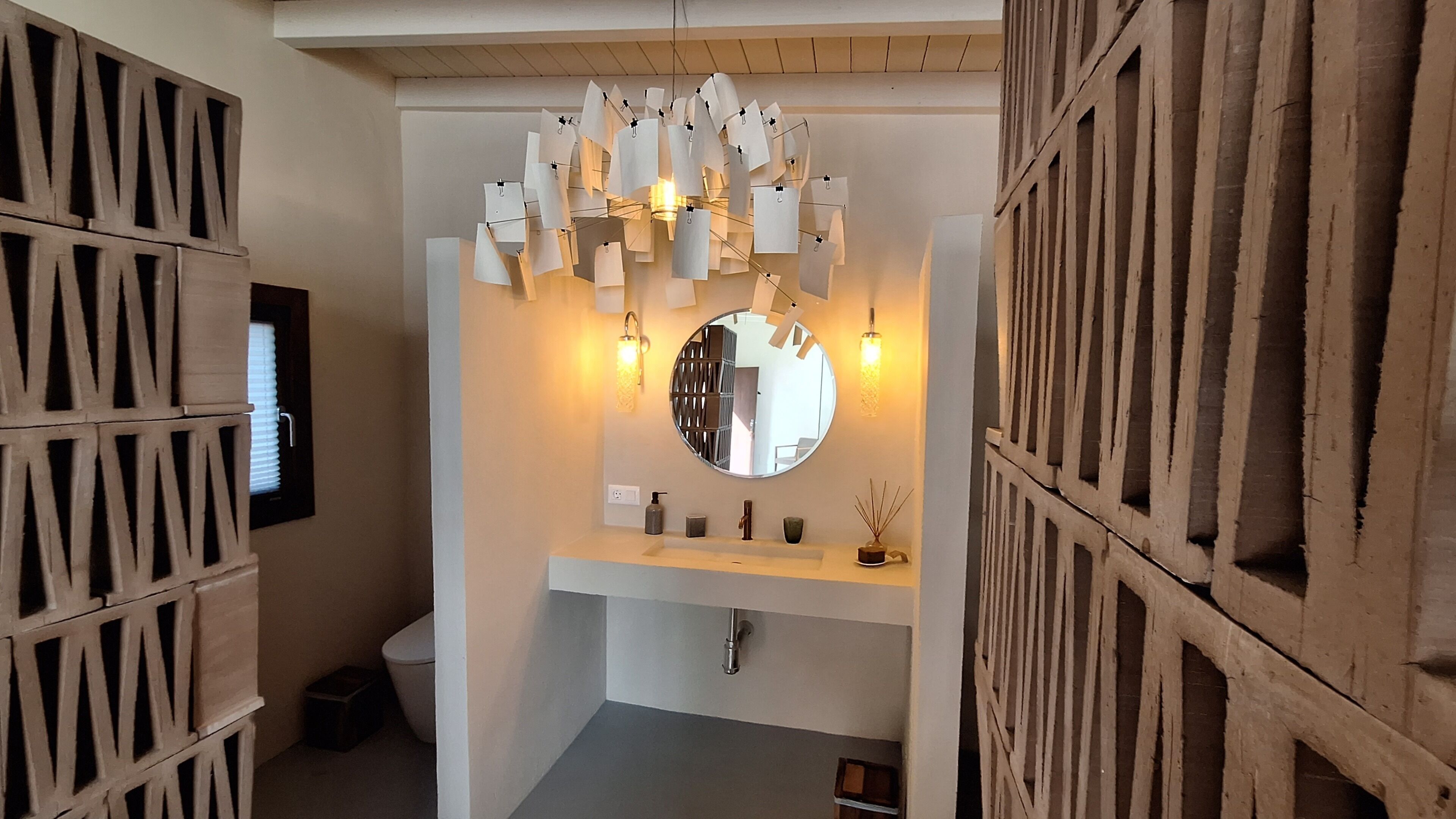 A bathroom with a modern sink, a round mirror, and a unique paper light fixture.