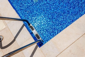 Ein Schwimmbecken mit klarem, blauem Wasser, einer Metallleiter und einem gefliesten Boden.