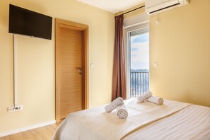 Ein Hotelzimmer mit einem Bett, einem an der Wand befestigten Fernseher, einer Tür und einem Fenster mit Vorhängen.