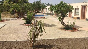 Une cour avec un chemin de gravier, des plantes en pot, un poteau métallique et un bâtiment doté d’un toit en tuiles.