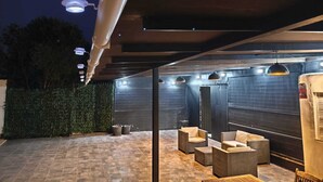 Une terrasse extérieure avec des sièges, un mur équipé de stores verticaux et un véhicule garé sur le côté.