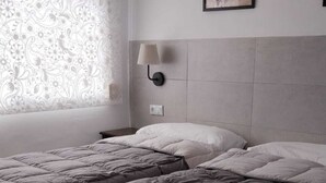 Une chambre à coucher avec un grand lit, une table de chevet, une lampe fixée au mur et un tableau encadré.