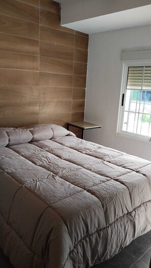 A bedroom with a large bed, a wooden headboard, a small bedside table, and a window with blinds. - El Rincón del Olivo (CARTAGENA)