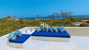 Eine Dachterrasse mit Blick aufs Meer, zwei blaue Sitzgelegenheiten und ein kleiner Pool im Hintergrund.