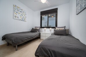 Une chambre avec deux lits simples, une table de chevet, une fenêtre avec vue et un ventilateur de plafond.