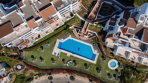 An aerial view of a resort with a central swimming pool, multiple lounge areas, and a circular water feature.