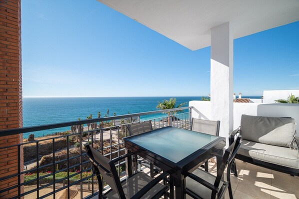 Un balcon avec une table et des chaises en verre, offrant une vue sur la côte.