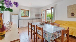 Un comedor con una mesa, sillas, un jarrón de flores y una cocina al fondo.