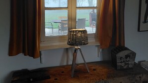 Ein Zimmer mit Fenster, Vorhängen, einer Stehlampe auf Stativ und einem kleinen Tisch mit einer Kiste.