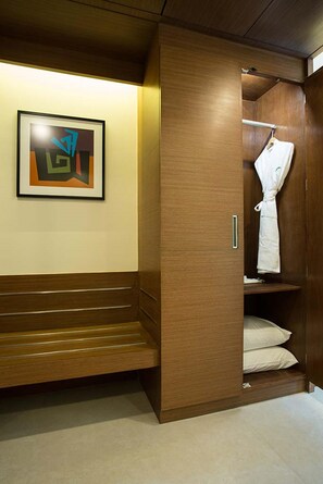 A wooden interior with a framed abstract painting, a robe hanging, and a bench. - The Fern Residency (Mumbai)