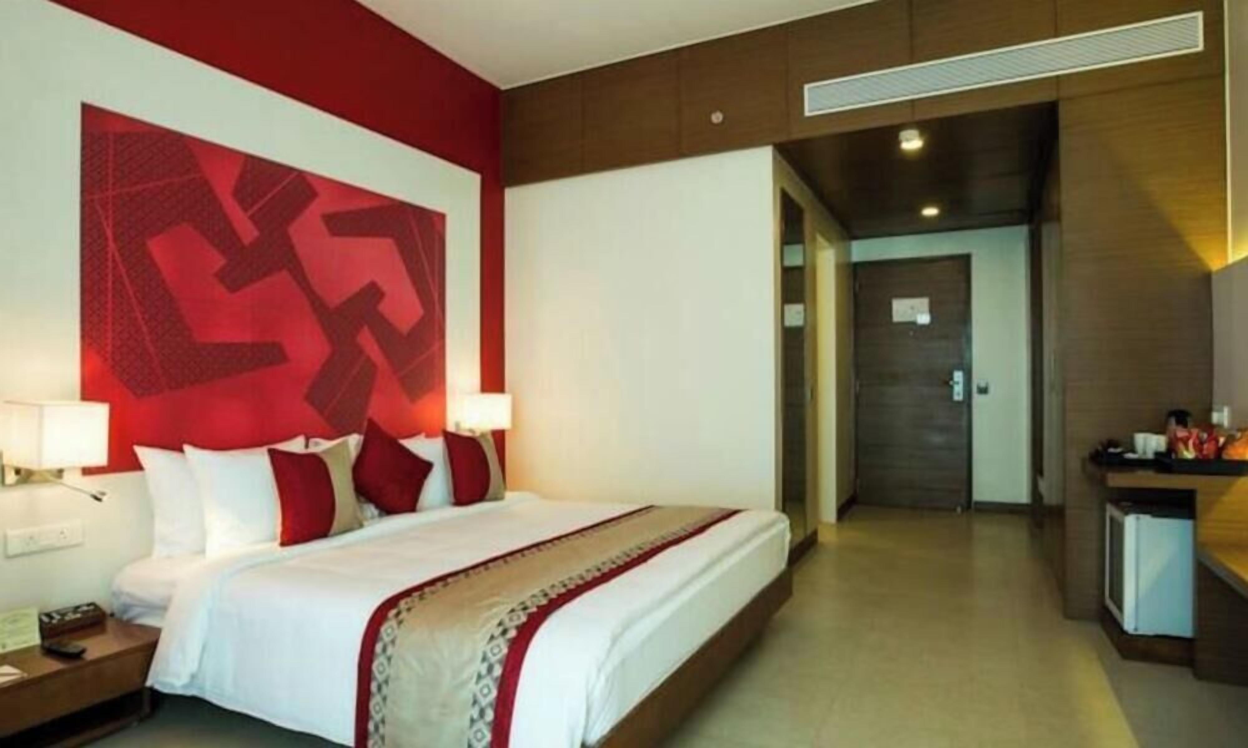 Ein Hotelzimmer mit einem großen Bett, Nachttischen, einem Schreibtisch und einer roten Akzentwand.