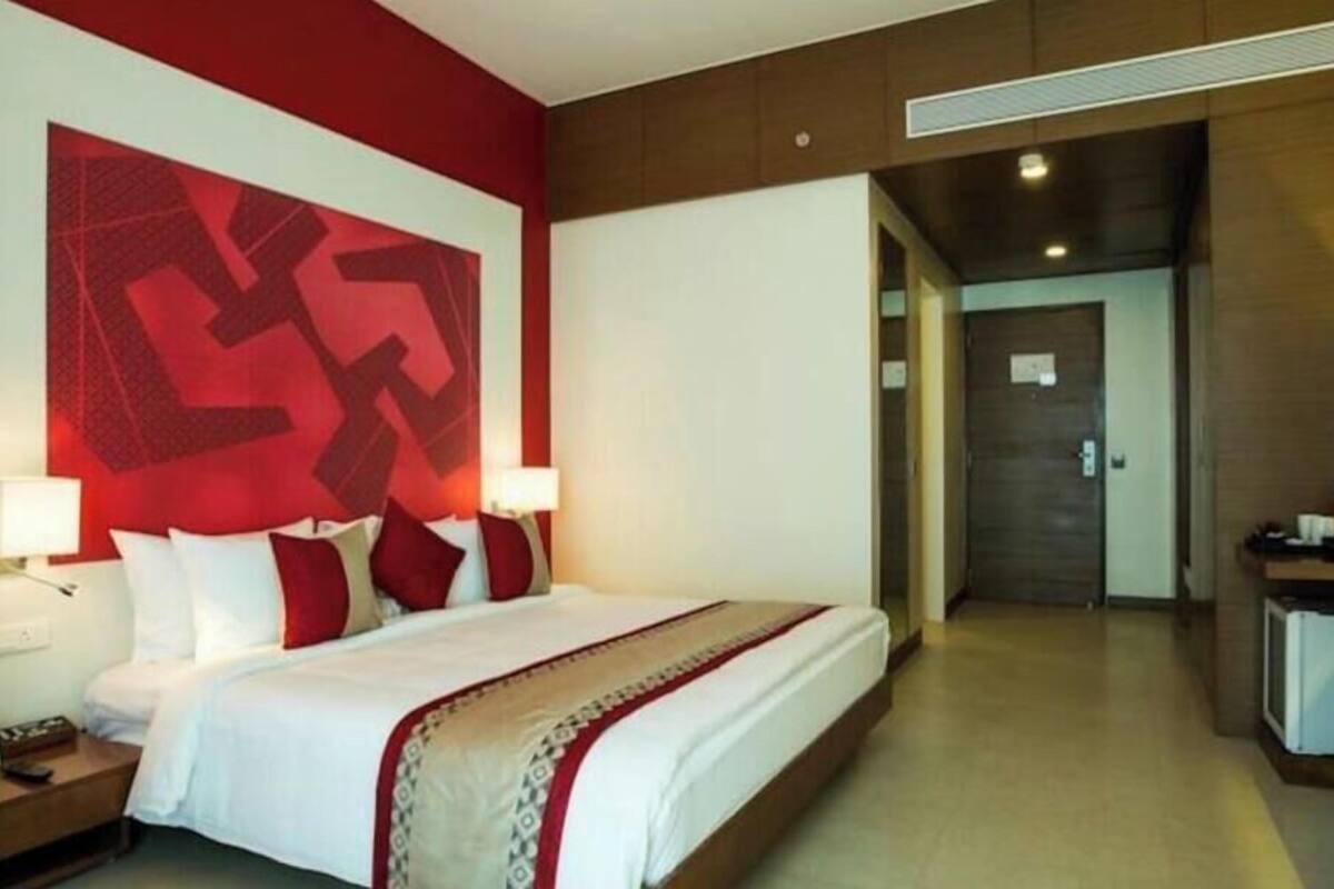 A hotel room with a large bed, bedside tables, a desk, and a red accent wall.