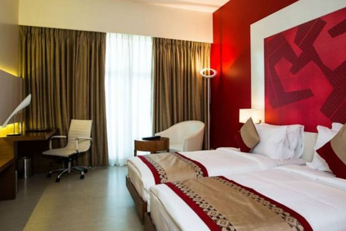 A hotel room with two beds, a desk, a chair, a TV, and a large window with curtains.