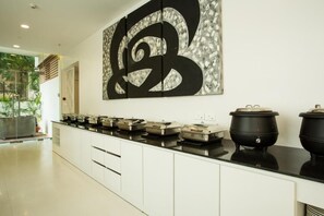 A modern kitchen with a long countertop, a large abstract art piece, and a pot on the right. - The Fern Residency (Mumbai)