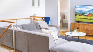 Moderni olohuone, jossa on harmaa kulmasohva, puinen sohvapöytä ja litteänäyttöinen televisio puisen lipaston päällä.