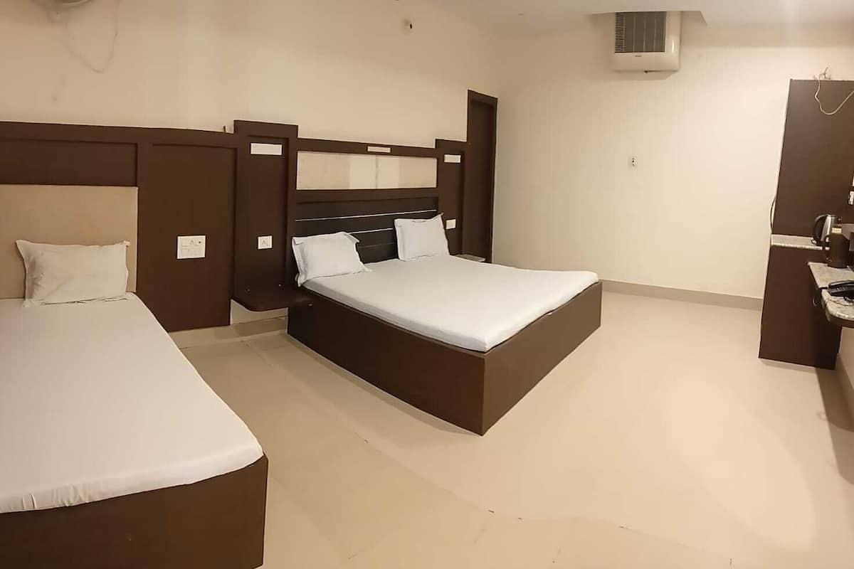 A hotel room with two beds, a large bed, a smaller bed, a bedside table, a chair, a desk, and a wall-mounted air conditioning unit.