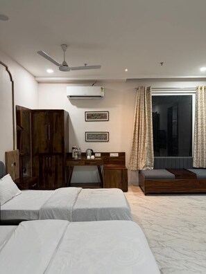 A hotel room with a bed, a desk, a wardrobe, and a large window with curtains. - The Utsav Hotel Unit of Rishabh Garden (Bikaner)