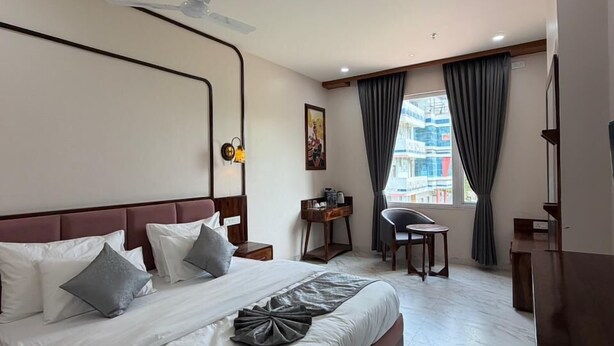 A hotel room with a large bed, a desk, a chair, a TV, and a window with curtains. - The Utsav Hotel Unit of Rishabh Garden (Bikaner)