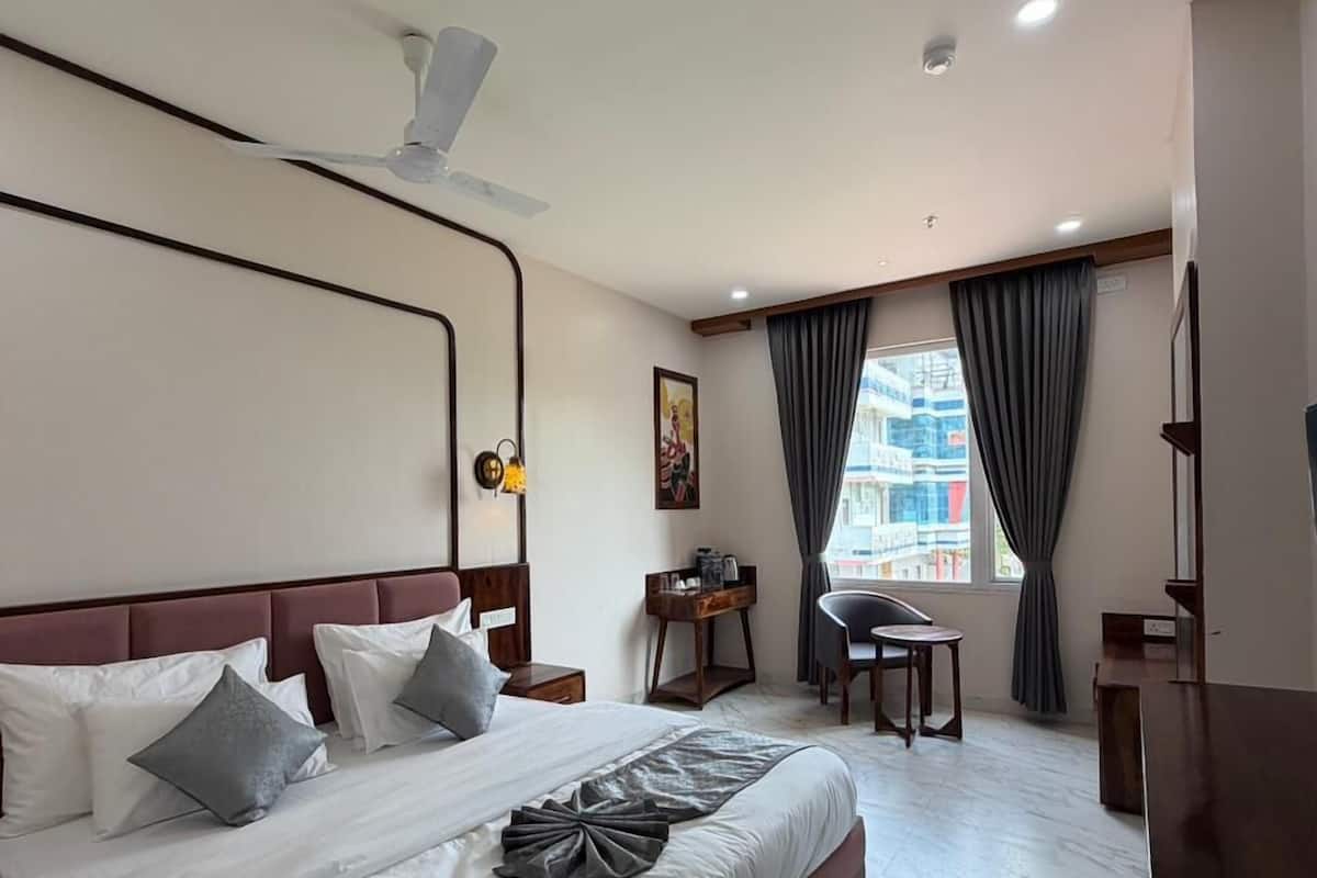 A hotel room with a large bed, a desk, a chair, a TV, and a window with curtains.