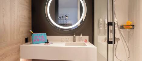 Une salle de bain moderne avec un meuble-lavabo, un miroir doté d'un anneau lumineux, une douche et des serviettes soigneusement pliées.