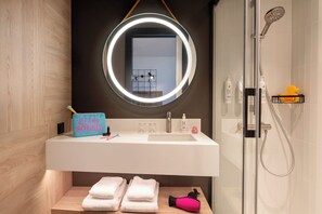 Un baño moderno con tocador, un espejo con luz de aro, ducha y toallas ordenadamente dobladas.