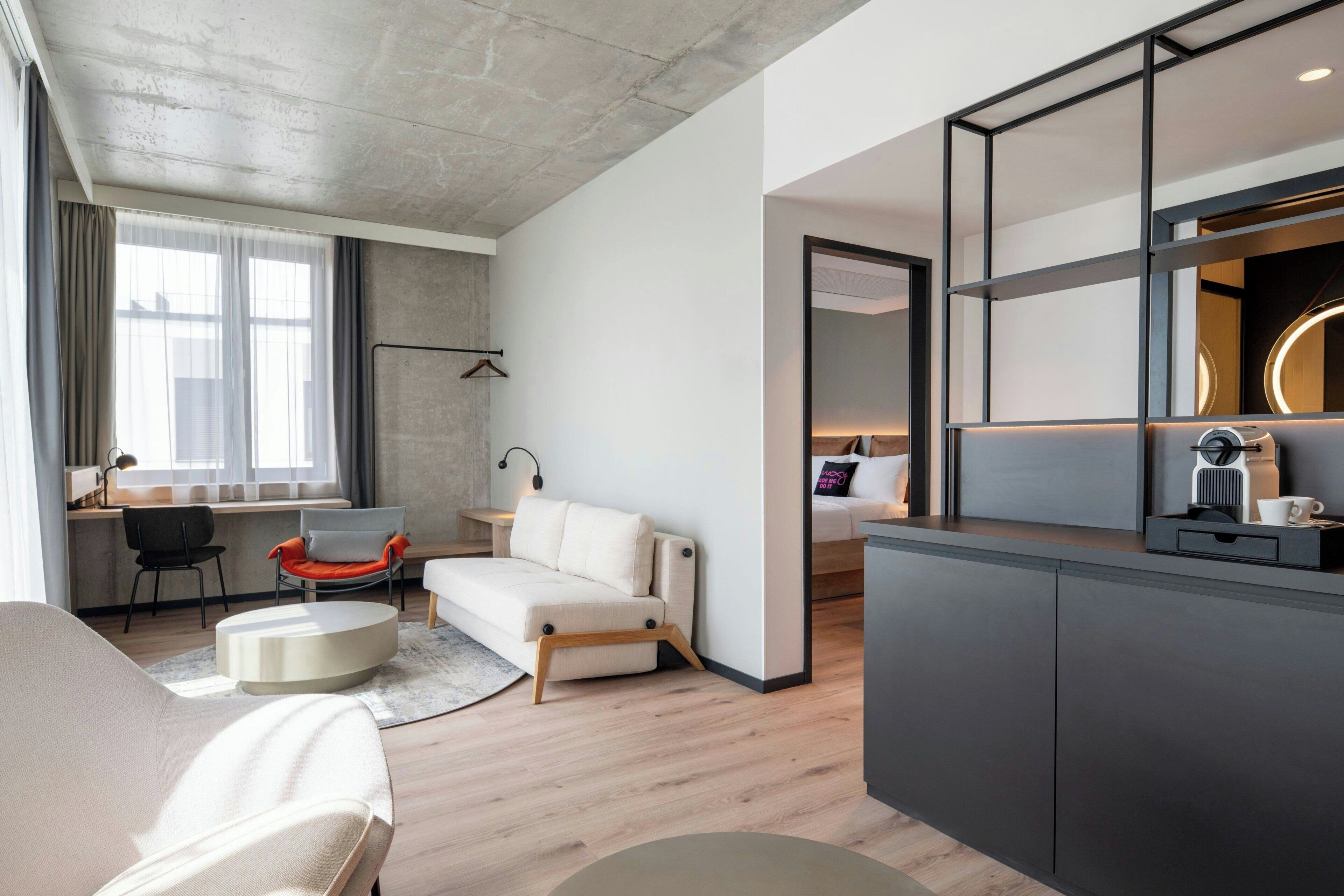 Una sala de estar moderna con un sofá, una mesa de centro, un escritorio y una zona de cocina con una cafetera.