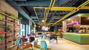 A modern hotel lobby with a reception desk, seating area, and shelves with plants. - Moxy Budapest Downtown (Budapest)