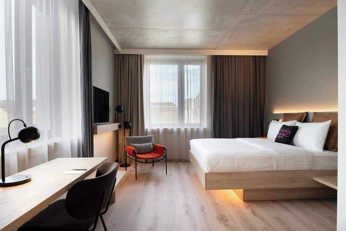 A hotel room with a bed, desk, chair, and a TV.