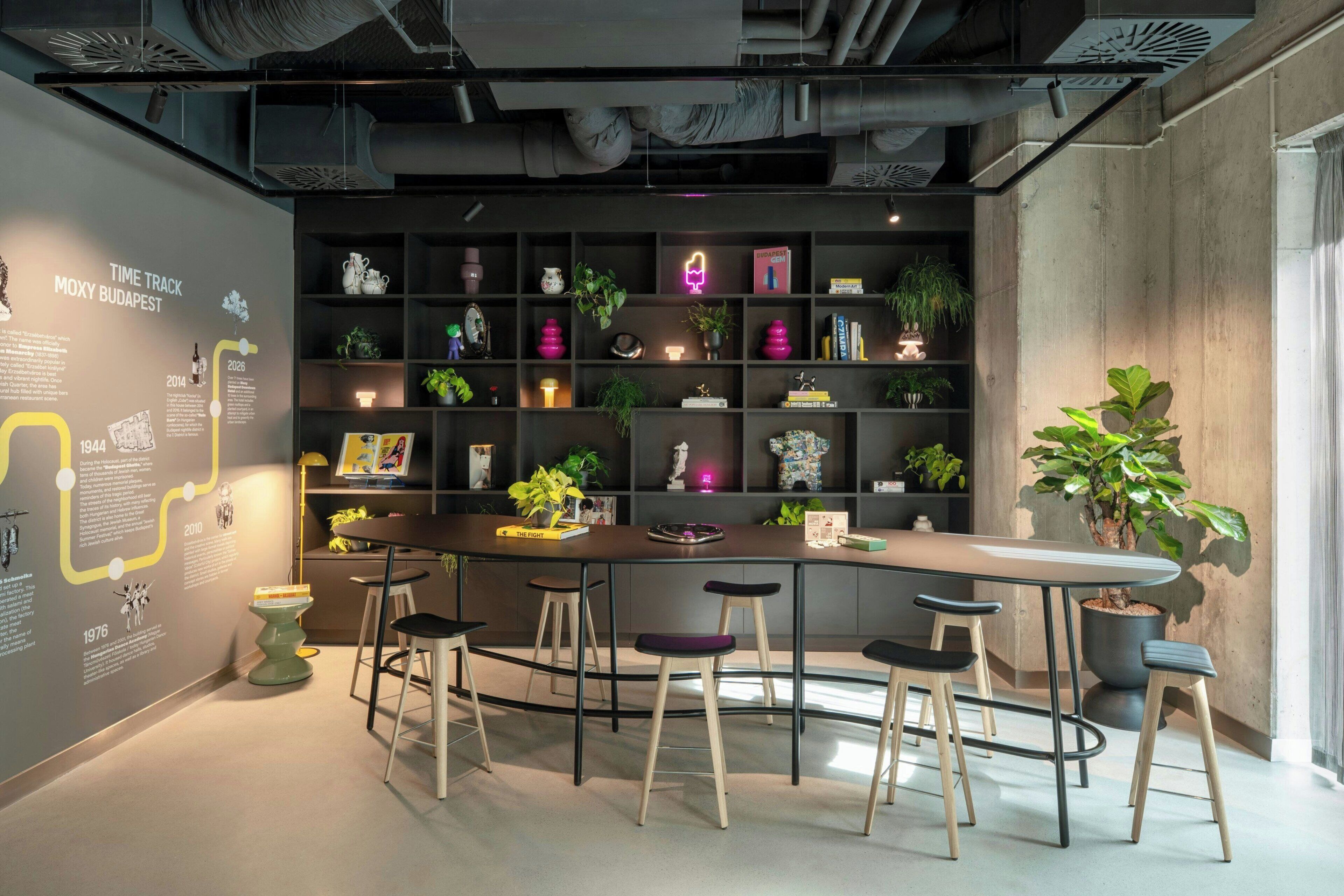 A modern bar area with a curved counter, stools, and shelves with plants and books.