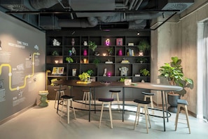 Una zona de bar moderna con una barra curva, taburetes y estantes con plantas y libros.