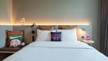Een hotelkamer met een bed, kussens, een nachtkastje, een lamp en een wandlamp.