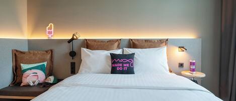 A hotel room with a bed, pillows, a bedside table, a lamp, and a wall-mounted light.