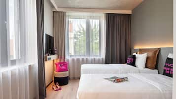Ein Hotelzimmer mit zwei Betten, einem Fernseher, einem kleinen Tisch und einem Fenster mit Vorhängen.